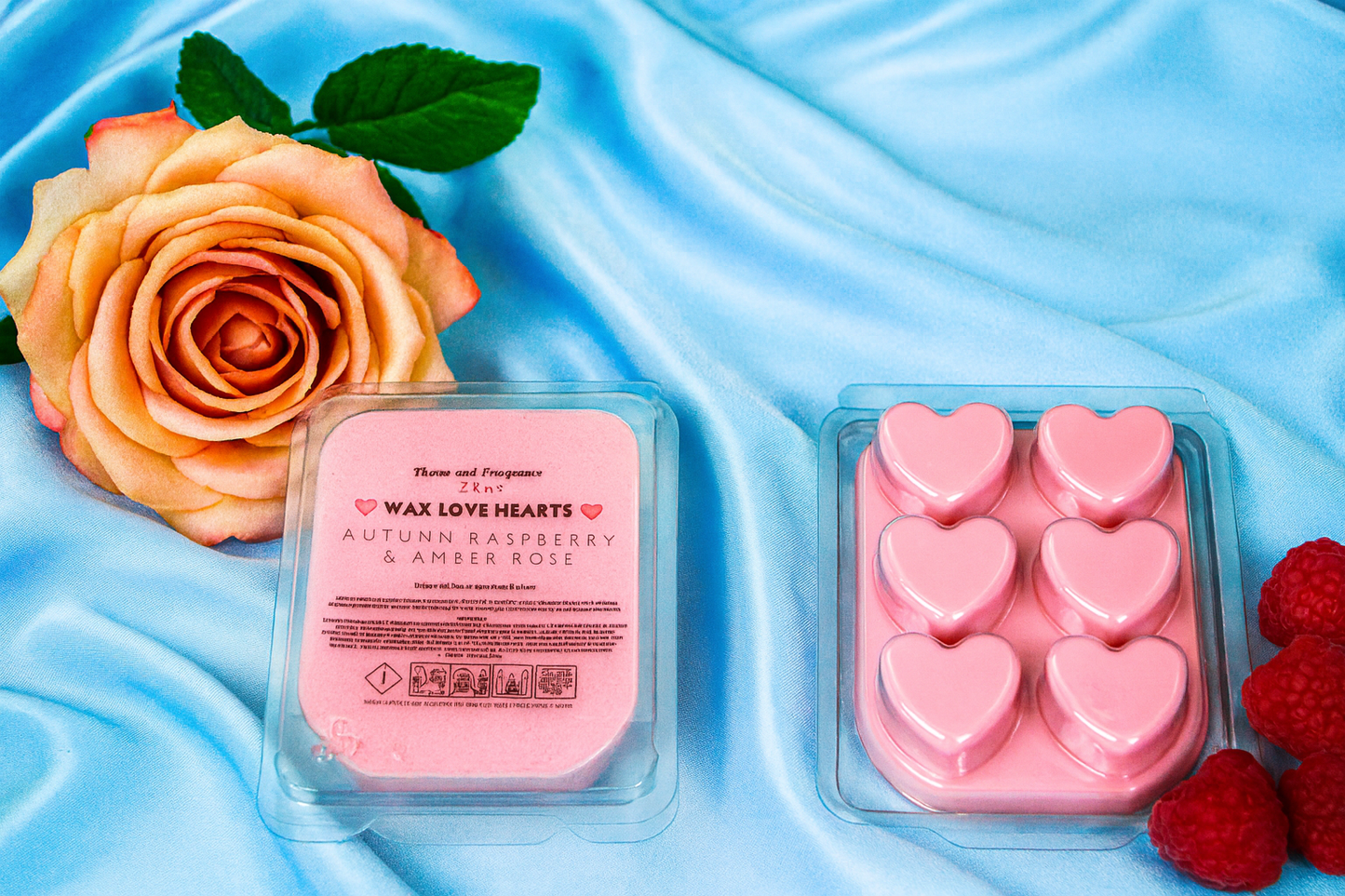Pink wax love hearts in a container with a rose and raspberries on a blue fabric background