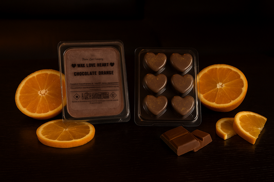 Heart-shaped chocolate orange fragranced Wax Melts with packaging and sliced oranges and chocolate pieces, on a dark background
