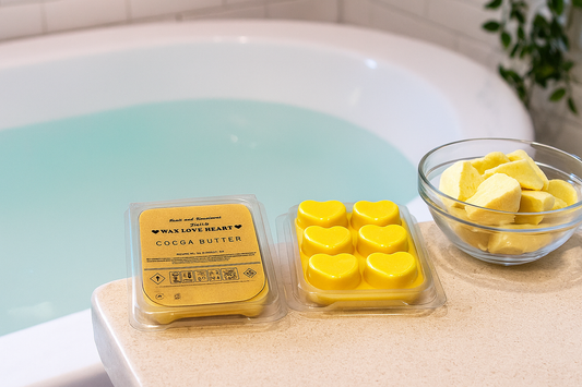 Yellow wax melts in heart shapes with packaging on a bathtub edge with a bowl of Cocoa Butter pieces.