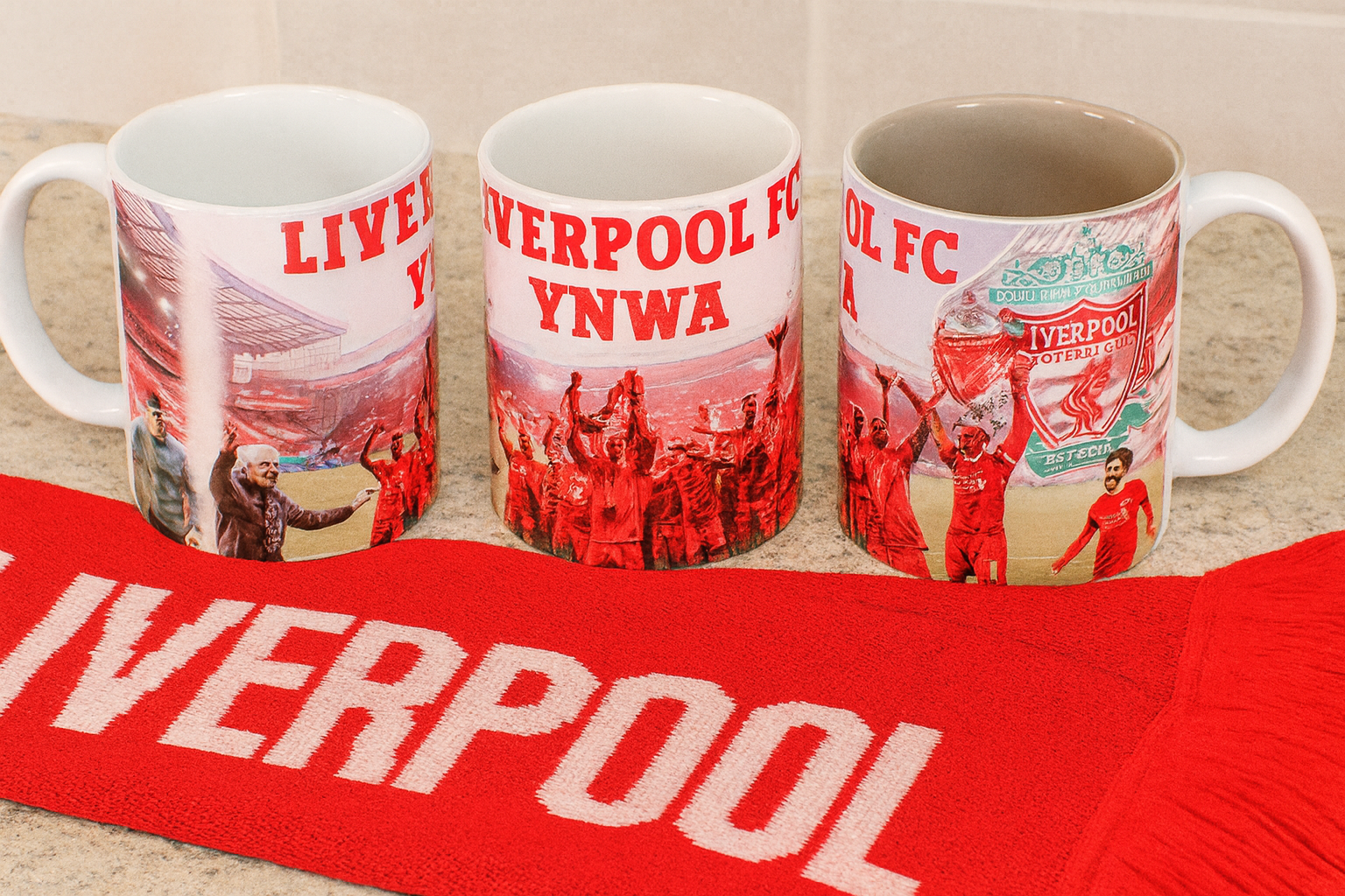 Three Liverpool FC mugs with a scarf featuring the word 'Liverpool' on a wooden surface.